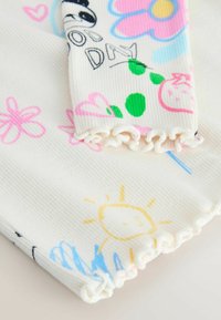 Material alb cu dungi, cu modele colorate de flori, un soare, inimioare și un panda, cu margini moi și ondulate la manșete.