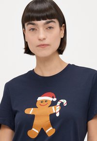 Camiseta de algodón azul marino con un gráfico de un hombre de jengibre que lleva un gorro de Navidad rojo y una caña de azúcar, destacando colores brillantes y formas simples.