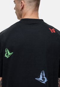 T-shirt in cotone nero con tre stampe di farfalle in rosso, verde e blu sul retro, con collarino rotondo e maniche corte.