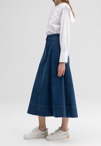 Bílé triko s volánkovým límcem a perlovými knoflíky, doplněné modrou denimovou sukní. Celý outfit dotvářejí pohodlné tenisky.