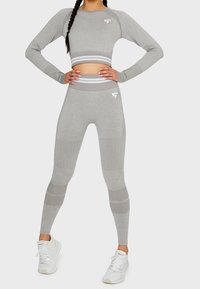 Grauer Crop-Top mit langen Ärmeln und gerippten Akzenten, kombiniert mit hochgeschnittenen grauen Leggings, die strukturierte Paneele und Muster aufweisen.