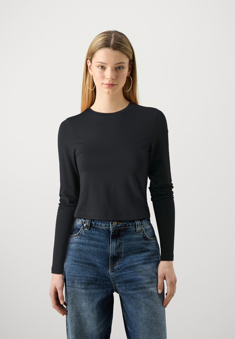 Svart langermet cropped topp laget av glatt stoff, kombinert med høyt liv blå denimjeans med en falmet design og fem lommer.