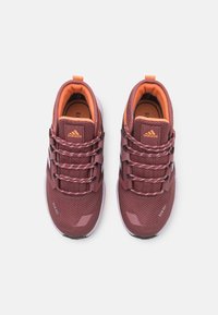 Viininpunaiset urheilukengät, joissa on rakenteellinen verkkopuoli, heijastavat yksityiskohdat ja oranssit korostukset. Varustettu helppokäyttöisellä nauhoitusjärjestelmällä ja pehmustetulla kauluksella.