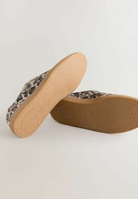 Paire de chaussures à enfiler imprimé léopard avec semelles en caoutchouc texturées de couleur marron clair, marquées "Next", posées sur une surface claire.