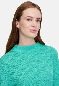 Strickpullover in Türkis mit einem strukturierten Muster, runder Ausschnitt, geripptem Saum und langen Ärmeln, der eine körpernahe Silhouette zeigt.