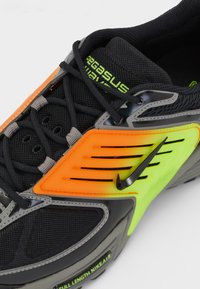 Nike Pegasus-skoene har en svart mesh-overdel med grå og oransje detaljer, en neon grønn swoosh, og en teksturert grå såle.