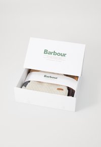Scatola rettangolare bianca con il logo "Barbour". All'interno, un maglione di lana piegato con strisce crema, blu navy e beige, con un piccolo tag del logo.