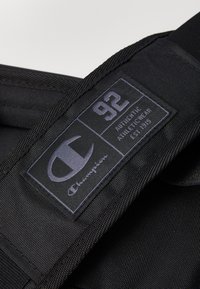 Black fabric label with white text featuring "92" and "Champion" logo, stitched on a textured, durable material.