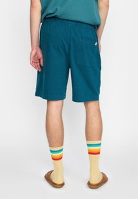 Teal shorts met een relaxed fit, elastische tailleband en een achterzak. Gedragen met beige gestreepte sokken met rode, gele en blauwe accenten.