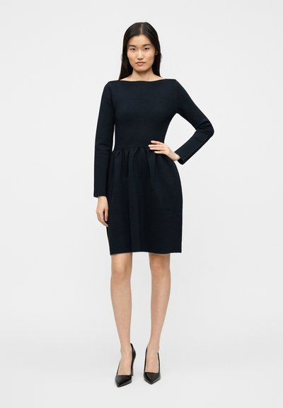 Μακρυμάνικο φόρεμα σε μπλε ναυτικό με λαιμόκοψη σκαφάκι, σούρα στη μέση και φουσκωτή φούστα. Το ύφασμα έχει διακριτικές ριγέ υφές. Συνδυάζεται με μαύρες γόβες.