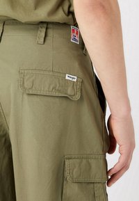 Olivově zelené cargo kalhoty s bočním kapsou a viditelným šitím. Na zadním pásu se nachází nášivka s logem Wrangler.