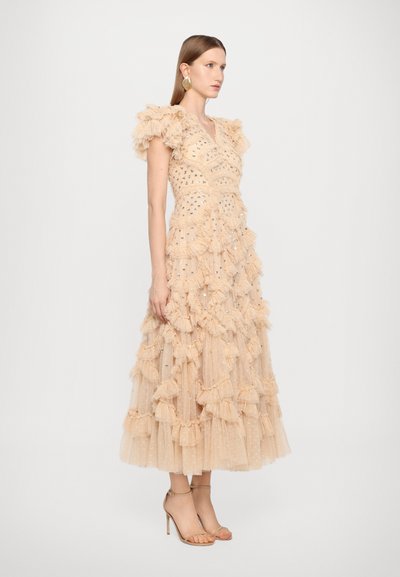 Robe en tulle pêche avec des manches à volants, des volants superposés et des embellissements dispersés, associée à des escarpins nude à lanières.