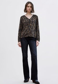 Blusa de estampado de leopardo marrón con escote en V y botones, combinada con vaqueros acampanados oscuros y botas negras de tacón. Tela suave y ligera.