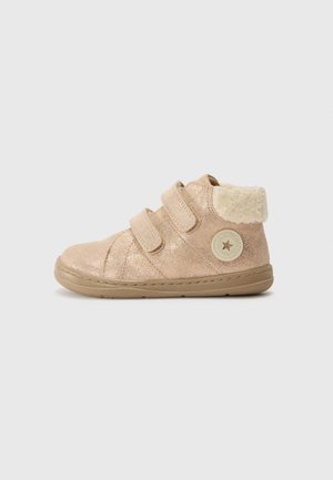 Botte beige pour tout-petit avec deux sangles en Velcro, semelle rembourrée et col en fourrure douce, ornée d'un patch logo rond sur le côté.