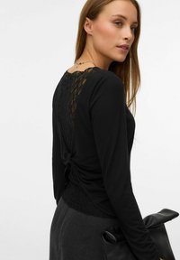 Crna majica dugih rukava s čipkastim panelom na leđima, od mekane teksturirane tkanine, s drapiranim dizajnom i suptilnim zavojem na leđima.