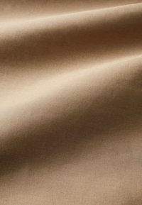 Tissu beige lisse avec de doux plis et une texture mate et douce, montrant un détail en gros plan du tissage du matériau.