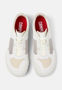 White sneakers with transparent mesh panels, textured cream accents, and white laces. Red insoles feature "CAMPER" branding. Rounded shape.