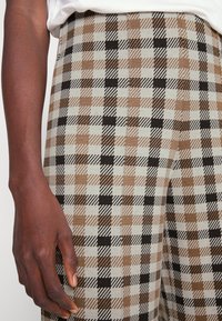 Bruine en zwarte geblokte broek met verschillende texturen. Casual fit en lichtgewicht stof, gecombineerd met een witte top.