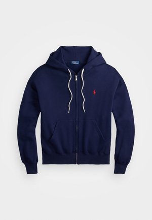 Námornícky modrá mikina na zips vyrobená z bavlny, s červeným logom na ľavej strane hrude, bielymi šnúrkami a predným klokanským vreckom.