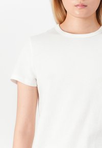 T-shirt bianca in cotone con maniche corte e scollatura rotonda. Texture liscia e design minimalista, che offre un aspetto pulito e semplice.
