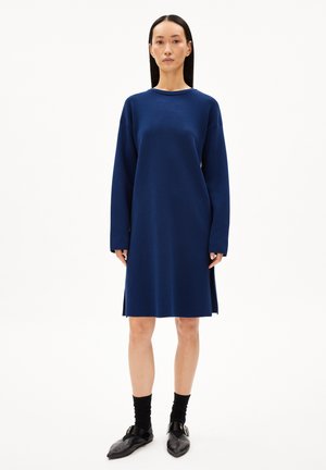 Abito lungo color blu navy, realizzato in tessuto morbido. Presenta una vestibilità ampia, scollo rotondo e spacchi laterali. Abbinato a scarpe nere e calze.