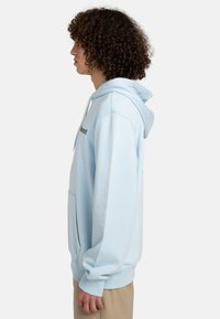 Light blue hoodie with a kangaroo pocket, drawstring hood, and side detailing in contrasting fabric. Soft cotton material, relaxed fit.