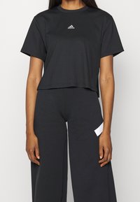 Svart ribbad, kortärmad t-shirt i bomull med rund halsringning och logotypdetalj på bröstet, kombinerad med löst sittande svarta byxor med en vit accent.