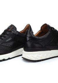 Zapatillas negras que combinan materiales de cuero y malla, con un diseño perforado, una suela geométrica blanca ligera y acentos de costura en contraste.