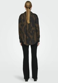 Camicia a maniche lunghe verde scuro con stampa nera, con orlo curvo e dettagli con bottoni sui polsini, abbinata a pantaloni neri a vita alta.
