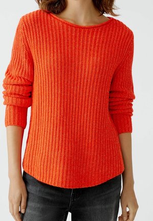 Pull en tricot orange vif avec une texture côtelée, encolure large et manches trois-quarts, associé à un jean foncé.