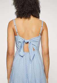 Modré květinové šaty s tenkými ramínky, mašlí na zadní straně a výřezem. Materiál má malý opakující se květinový vzor.