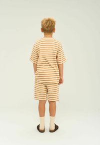Randig beige t-shirt och matchande shorts, med horisontella ränder i en mörkare nyans av beige, kombinerat med ljusa strumpor och mörka skor.