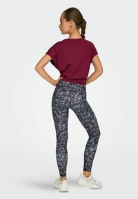 Vinröd kortärmad topp och blommönstrade, figurnära leggings. Leggingsen har en mörk bakgrund med flerfärgade blommor. Vita sneakers.