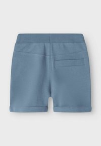 Jasnoniebieskie szorty z fakturowanej tkaniny, z podwiniętymi nogawkami i ściągaczem w pasie. Posiadają tylną kieszeń do przechowywania.