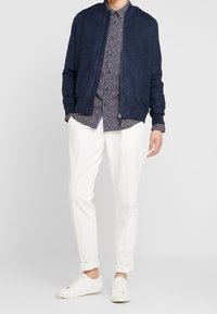 Námořnická sukně bomber, vzorovaná košile s tmavým pozadím, off-white oblečené kalhoty a bílé tenisky.