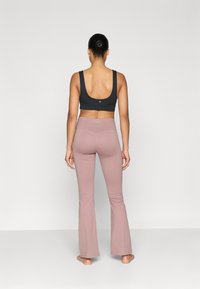 Black sports bra with wide straps, paired with light pink flared leggings. The fabric has a smooth texture and a fitted design.