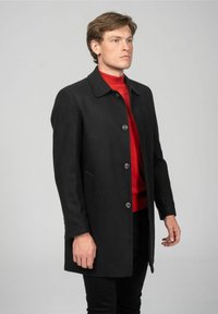 Zwarte wollen jas met een rechte snit, voorzien van een kraag, knopen aan de voorkant en zijzakken. Draag het over een rood coltrui.