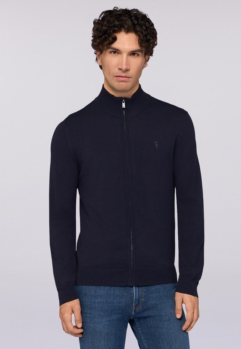 Námorní zipový svetr vyrobený z hladkého materiálu, s vysokým límcem a dlouhými rukávy, s ribovanými lemy a malým logem na hrudi.