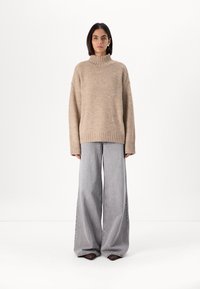 Beige knitted turtleneck sweater with wide sleeves, paired with light gray wide-leg jeans and pointed-toe black shoes.