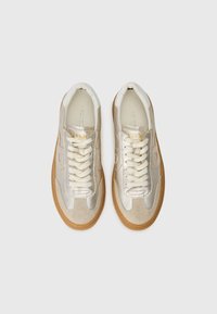 Baskets beige et dorées avec dessus en daim texturé et en cuir lisse, dotées de lacets crème et d'une semelle en gomme.