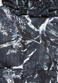 Černá a šedá zateplená bunda s podrobným lesním maskovacím vzorem, který obsahuje větve, listy a kapuci se stahovací šňůrkou.