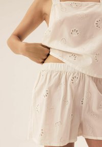 White cotton two-piece set featuring a sleeveless top and shorts. Both pieces have embroidered accents and cut-out details throughout.