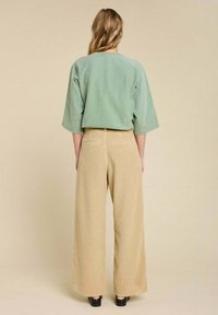 Un haut oversized vert menthe avec des manches trois quarts porté avec un pantalon large en velours côtelé beige, présentant une texture côtelée et des poches arrière.