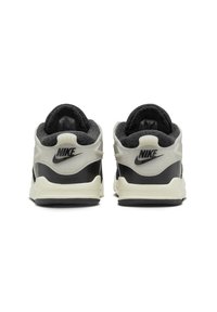 Des baskets Nike en noir et crème. Elles possèdent des cols rembourrés, des textures variées et des accents de logo sur le talon. Les semelles en caoutchouc offrent une bonne adhérence.