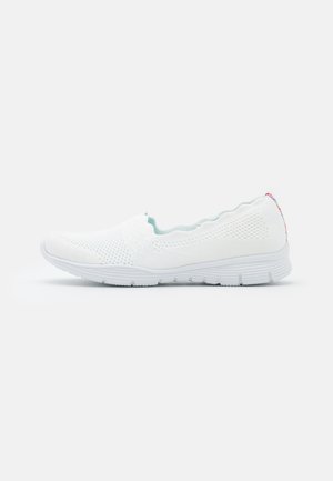 Zapatos blancos sin cordones con parte superior de punto texturizado, cuello ondulado y suela de goma flexible con sutiles acentos en tonos pastel en el talón.