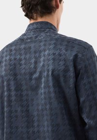 Donkerblauwe shirt met een gestructureerd houndstooth-patroon. De stof heeft een gladde glans en een klassieke kraagontwerp.