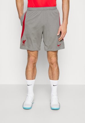 Mann trägt graue Liverpool FC Sportshorts mit roten Seitenstreifen, weiße Nike-Socken und weiße Sportschuhe mit blauen Sohlen.