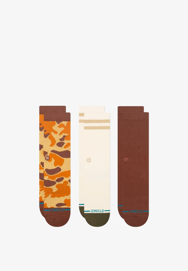 Trois paires de chaussettes : l'une arbore un motif camouflage marron et orange, une autre est crème avec des rayures beige, et la dernière est unie marron, toutes avec des accents de logo.