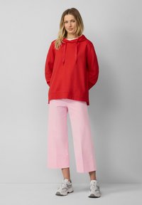 Rode hoodiesweater met koordjes, gecombineerd met lichtroze wijde broek. Witte t-shirt eronder, grijze sneakers met accenten.