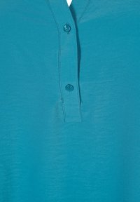 Türkisfarbenes Shirt mit V-Ausschnitt und drei Knöpfen an der Vorderseite. Der Stoff ist glatt und leicht und zeichnet sich durch ein einfaches, ungeschmücktes Design aus.